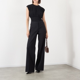 Model wearing Anine Bing black sleeveless ruched viscose top with wide-leg black trousers and brown mini shoulder bag.