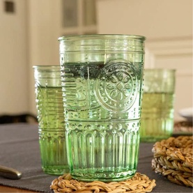 Set of green embossed glass tumblers with decorative relief patterns, styled on a grey surface with woven placemats