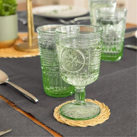 Green embossed glass goblet with floral medallion and ribbed detail, on rattan coaster, with matching glasses in background
