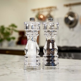 Cole & Mason clear acrylic salt and pepper mill set displayed on a marble kitchen countertop, with pots visible in background