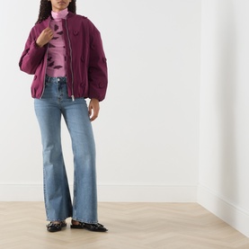 Model wearing Fabienne Chapot Hearty 3D Heart Appliqu&eacute; Bomber Jacket in Brigitte Bordeaux, styled with a pink turtleneck and light blue flared jeans.