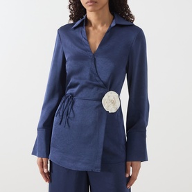 Model wearing Fabienne Chapot Maritime Blue wrap shirt with white rosette detail, long sleeves, and tie waist, styled with matching trousers.