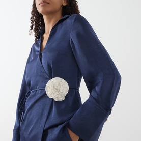 Model wearing Fabienne Chapot Maritime Blue satin shirt with wrap silhouette and white floral corsage detail at waist.