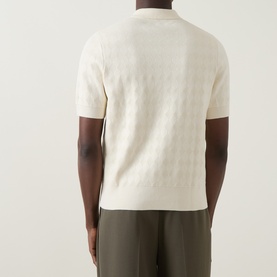 Model wearing cream textured knit short-sleeve polo shirt, styled with olive trousers, back view