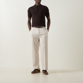 Model wearing Fred Perry Laurel Wreath Logo Polo Shirt in Rich Brown with cream wide-leg trousers and brown suede trainers.