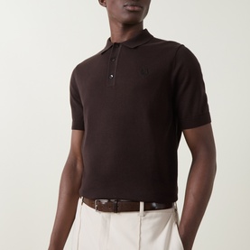 Model wearing Fred Perry Laurel Wreath Logo Polo Shirt in Rich Brown, short sleeves, polo collar with button fastenings, styled with cream trousers