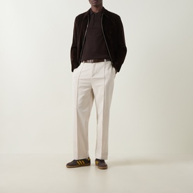Model wearing Fred Perry Laurel Wreath Logo Polo Shirt in Rich Brown, styled with dark zip jacket, cream trousers and brown trainers.