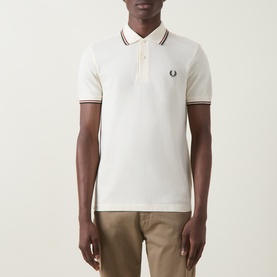 Model wearing Fred Perry Laurel Wreath Logo Twin Tipped Polo Shirt in Ecru with brandy and green tipped collar and cuffs, styled with chino trousers.