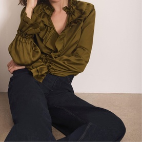 Model wearing Mint Velvet green satin ruffle V-neck blouse with gathered sleeves, styled with dark navy wide-leg jeans