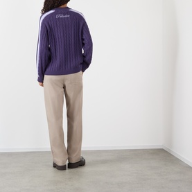 Model wearing Pellador purple cable-knit cotton jumper with white stripe sleeve detail, styled with beige wide-leg trousers, back view.