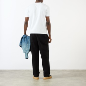Model wearing Pellador white cotton T-shirt, back view, styled with black trousers and tan shoes, holding a denim jacket