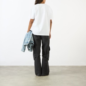 Model wearing Pellador Pigeon Fancier Graphic T-Shirt in white, styled with dark cargo trousers and carrying a denim jacket.