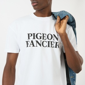 Model wearing Pellador white cotton T-shirt with Pigeon Fancier slogan print, styled with a denim jacket draped over one shoulder.