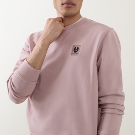Model wearing Belstaff Logo Badge Sweatshirt in Dusk Pink, crew neck with V-shaped insert and Phoenix logo badge on chest.
