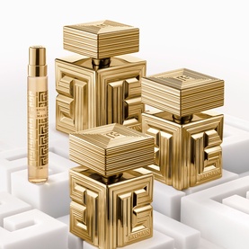 Balmain Parfum collection in gold geometric cube-shaped bottles with ribbed detailing, including a slim rollerball, on white geometric surface