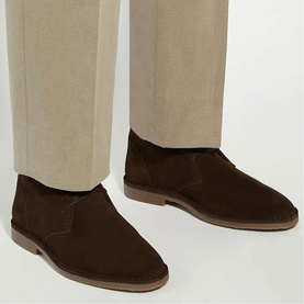 Model wearing dark brown suede slip-on desert shoes with tan crepe sole, styled with cream tailored trousers