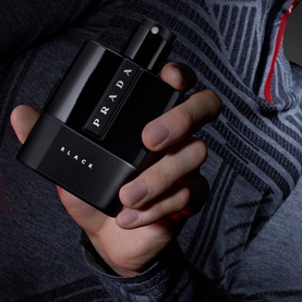 Prada Luna Rossa Black eau de parfum, sleek black rectangular bottle with silver cap, held in hand against grey clothing