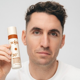 Model with Solas Skin Solas Spritz SPF 30 Face Mist, holding white and red aerosol sunscreen bottle close to face