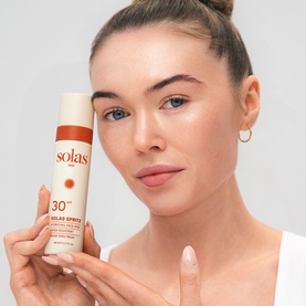 Solas Skin Solas Spritz SPF 50 Face Mist spray bottle held on a palm, cream and terracotta packaging with sun motif