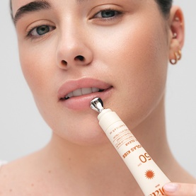 Model with Solas Skin lip sun care product, applying roller-tip SPF lip balm tube to lips