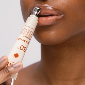 Model with Solas Skin Solar Kiss SPF50 lip sunscreen, shown applied to lips using metal roller-ball applicator tip