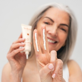 Model with Solas Skin SPF suncare, showing three swatches of cream formula on fingers, holding tube against light background