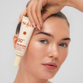 Model with Solas Skin SPF 50 sun care tube held to forehead, showcasing product application on bare skin