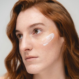 Model with Solas Skin SPF applied as a white cream swatch beneath the eye, shown on fair freckled skin with natural lighting.
