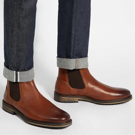 Model wearing tan leather Chelsea boots with elastic side panels and dark brown sole, styled with cuffed dark indigo jeans
