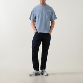 Model wearing Belstaff Mist Blue crew neck cotton T-shirt, styled with dark navy cargo trousers and grey trainers.