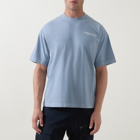 Model wearing Belstaff Mist Blue cotton crew neck T-shirt with small chest logo print, styled with dark trousers.