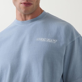 Model wearing Belstaff Crew Neck T in Mist Blue cotton, featuring embossed logo print at chest, close-up detail shot.