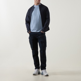 Model wearing Belstaff Mist Blue Crew Neck T, styled with navy zip-up jacket, navy cargo trousers and grey trainers.