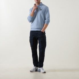 Model wearing Belstaff Mist Blue cotton half zip sweatshirt, styled with dark navy cargo trousers and white trainers.