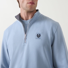 Model wearing Belstaff Mist Blue cotton half-zip sweatshirt with silver zip and branded patch logo on chest.