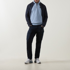 Model wearing Belstaff Mist Blue cotton half-zip sweatshirt, styled with navy quilted jacket, navy cargo trousers and grey trainers.