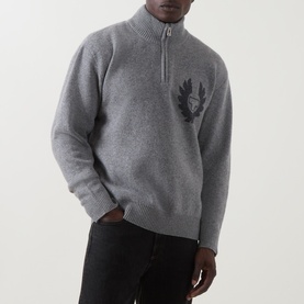 Model wearing grey half-zip knit jumper with embroidered crest logo on chest, styled with dark trousers
