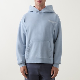 Model wearing Belstaff Mist Blue cotton hoodie with kangaroo pocket and small chest logo print, paired with grey trousers.
