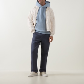 Model wearing Belstaff Mist Blue cotton hoodie, styled with cream quilted jacket, navy trousers and white trainers.