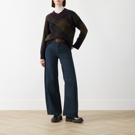 Model wearing Barbour Shadow Classic Tartan wool argyle V-neck jumper, styled with wide-leg dark jeans and brown belt.