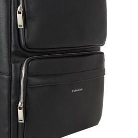 Calvin Klein black backpack close-up showing front zip pockets and silver-tone hardware detailing with logo badge.