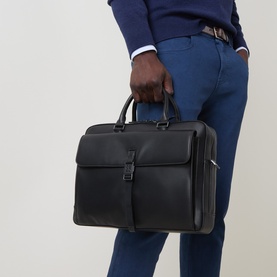 Model carrying Calvin Klein Commuter Logo Briefcase in black with gunmetal hardware, engraved buckle front pocket and top handles. Styled with blue