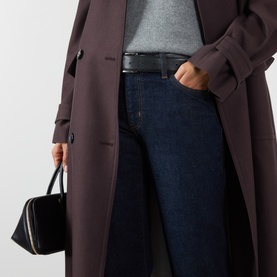 Model wearing FRAME DENIM Slim jeans in Rinse dark indigo wash, styled with a brown longline coat and black leather belt.