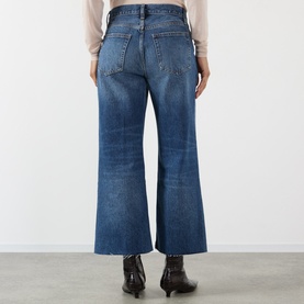 Model wearing FRAME DENIM Wide Leg Jeans in Lucky Raw After blue denim, rear view, styled with a beige top and black western ankle boots.