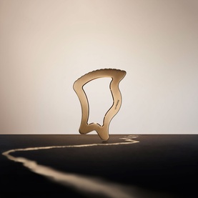 La Prairie Firm/Tone Treatment displayed as abstract golden sculptural form casting a curved shadow on dark surface
