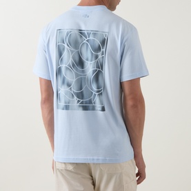 Model wearing Lacoste Crew Neck T in light blue, rear view showing large graphic print of overlapping circles on back.