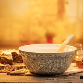 Grey ceramic mixing bowl with embossed floral pattern and wooden spoon, styled on rustic surface with cinnamon sticks and cake