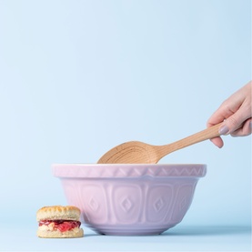 Mason & Cash pink mixing bowl with wooden spoon, styled with a cream scone, hand shown placing spoon into bowl