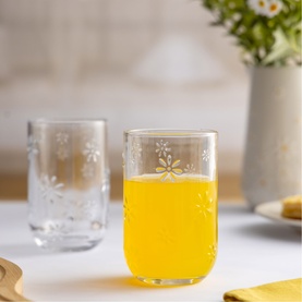 Ravenhead clear glass tumblers with etched daisy pattern, one filled with orange juice, styled on a white table with flowers