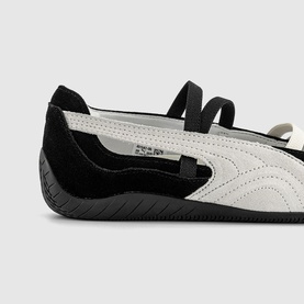 Puma black and white leather ballet flat shoe with elastic strap, black suede heel panel and black rubber sole, close-up detail view.